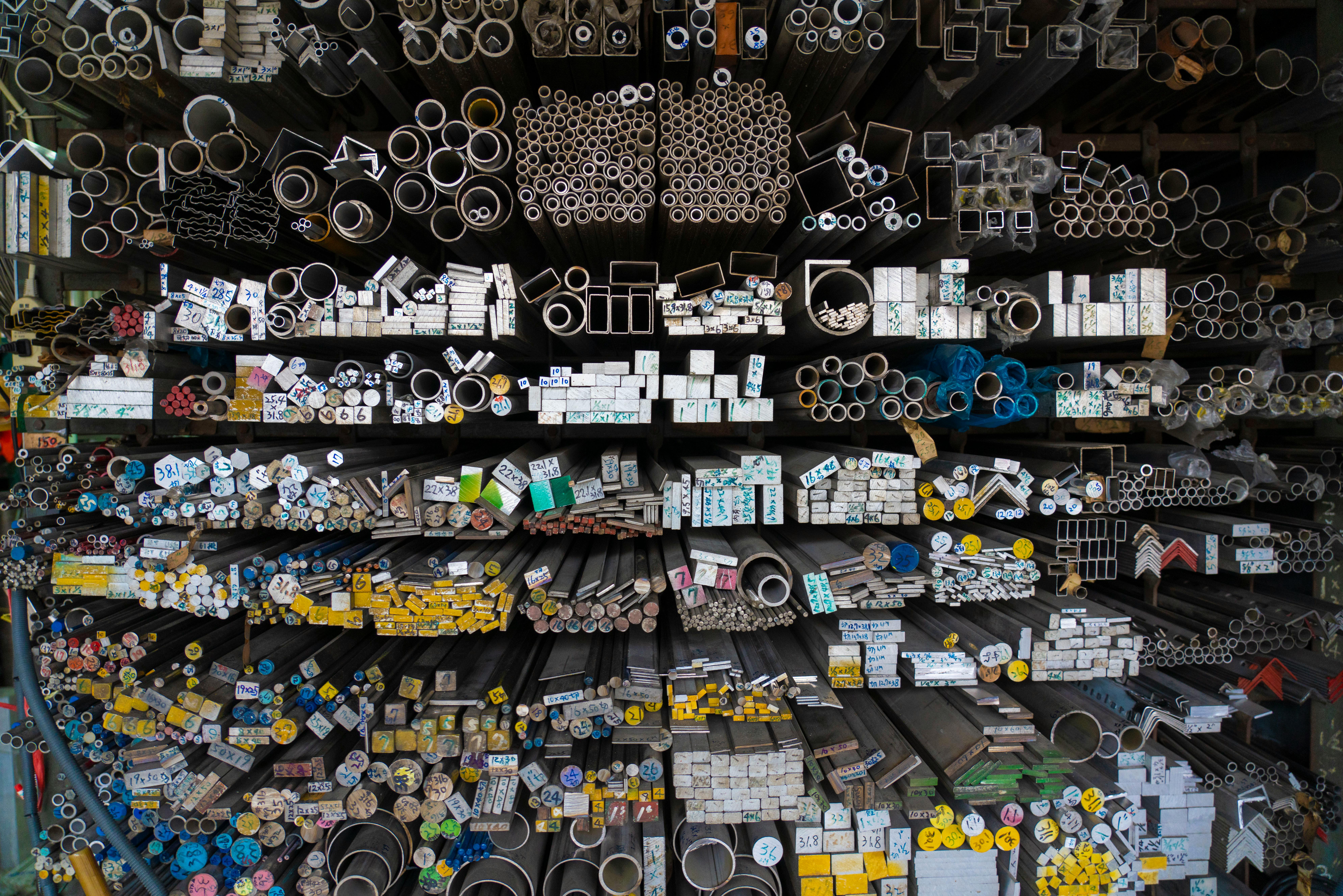 Diverse collection of stacked metallic pipes and rods in a warehouse display.